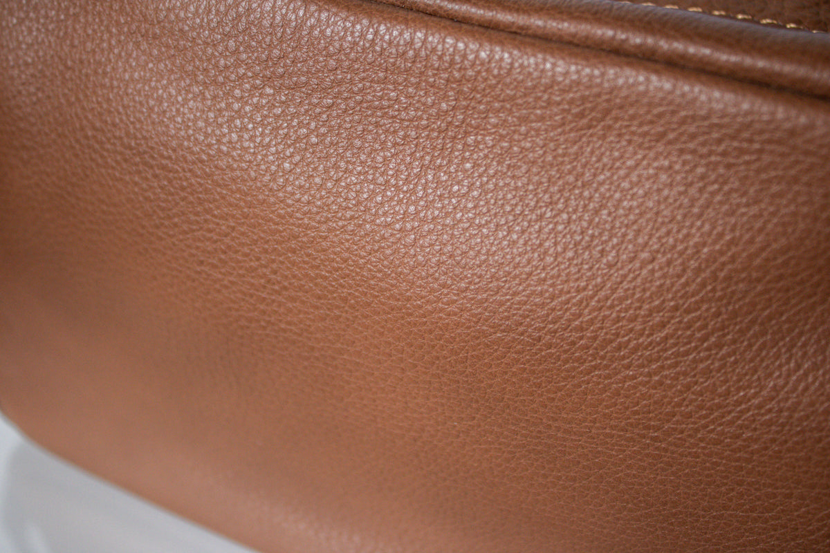 Close-up of a brown pebbled leather Dopp bag, with a zipper edge visible at the top.