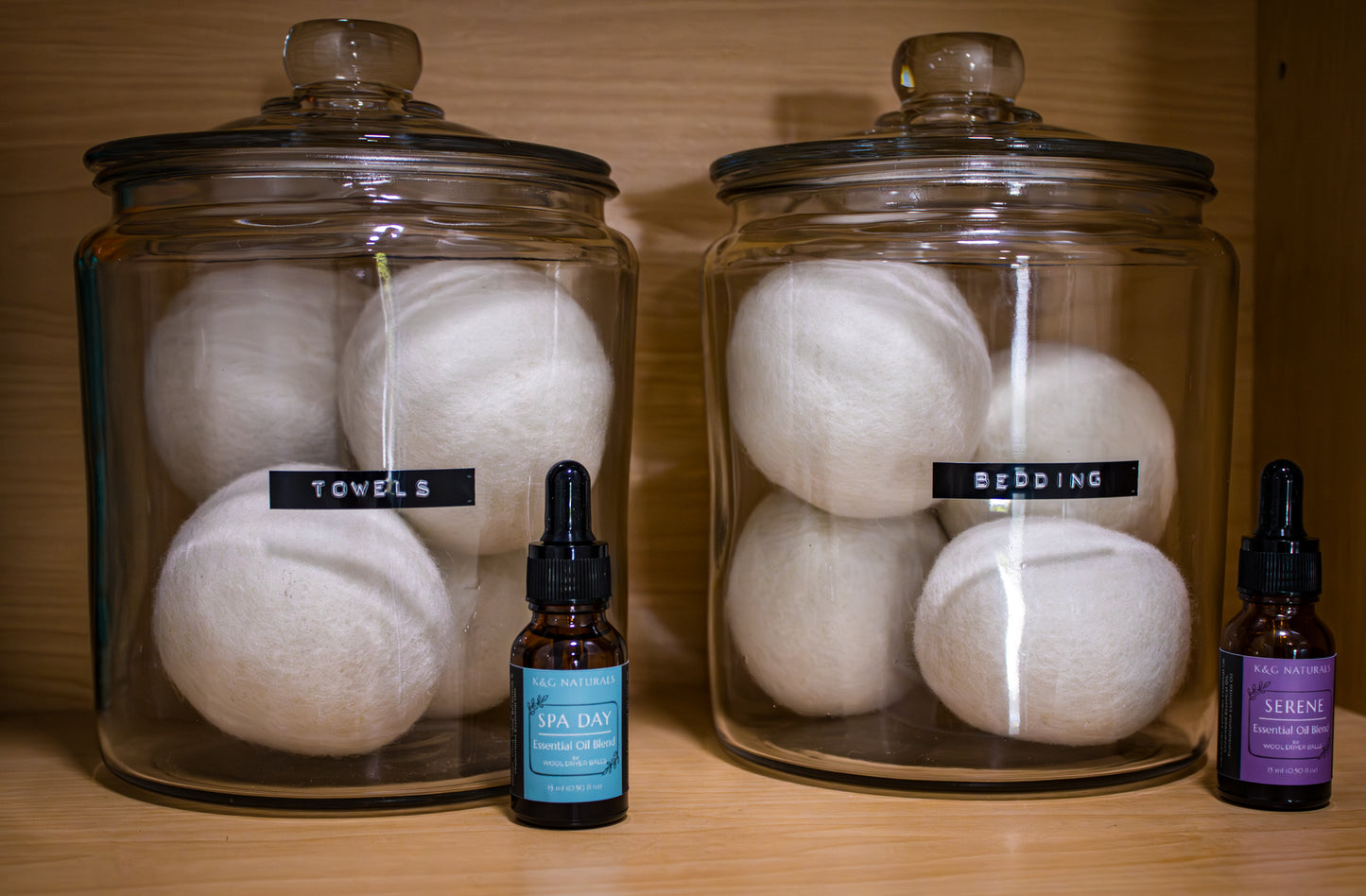 Two glass jars with labels on a wooden surface, accompanied by two bottles of K&G Naturals dryer ball blends dropper bottles.