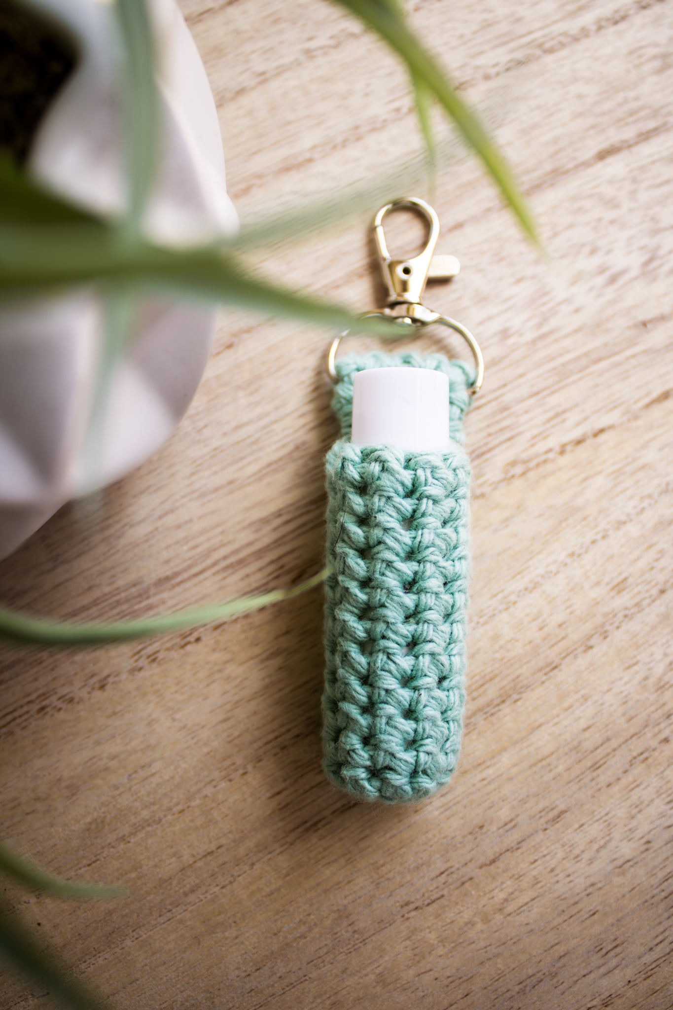 Jade green crocheted chapstick holder keychain with a white chapstick tube in it on a wooden surface