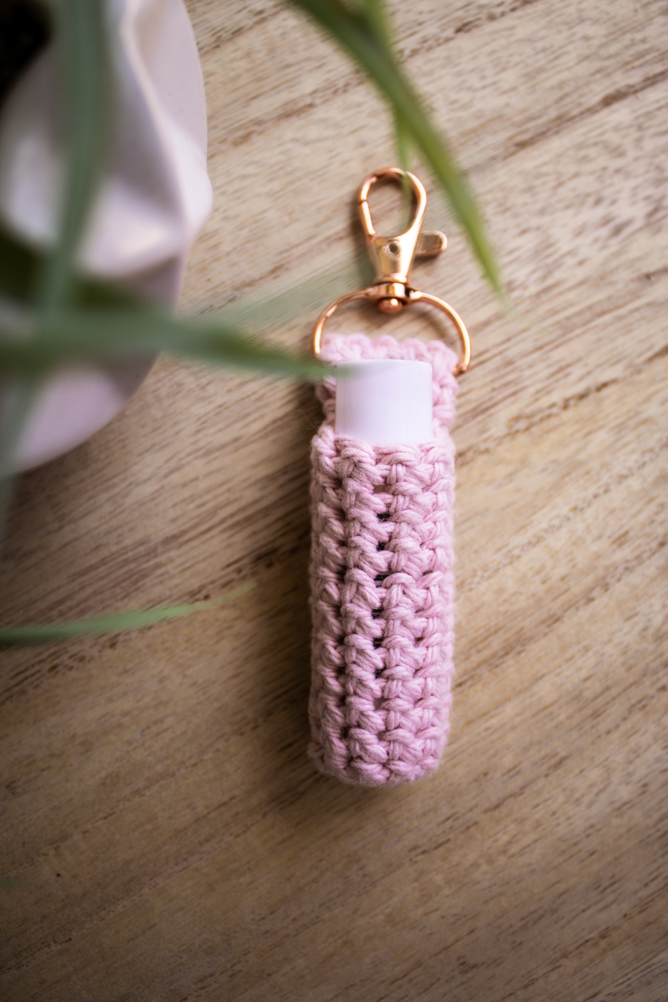 Rose colored chapstick holder keychain with a rose gold clasp on a wooden surface