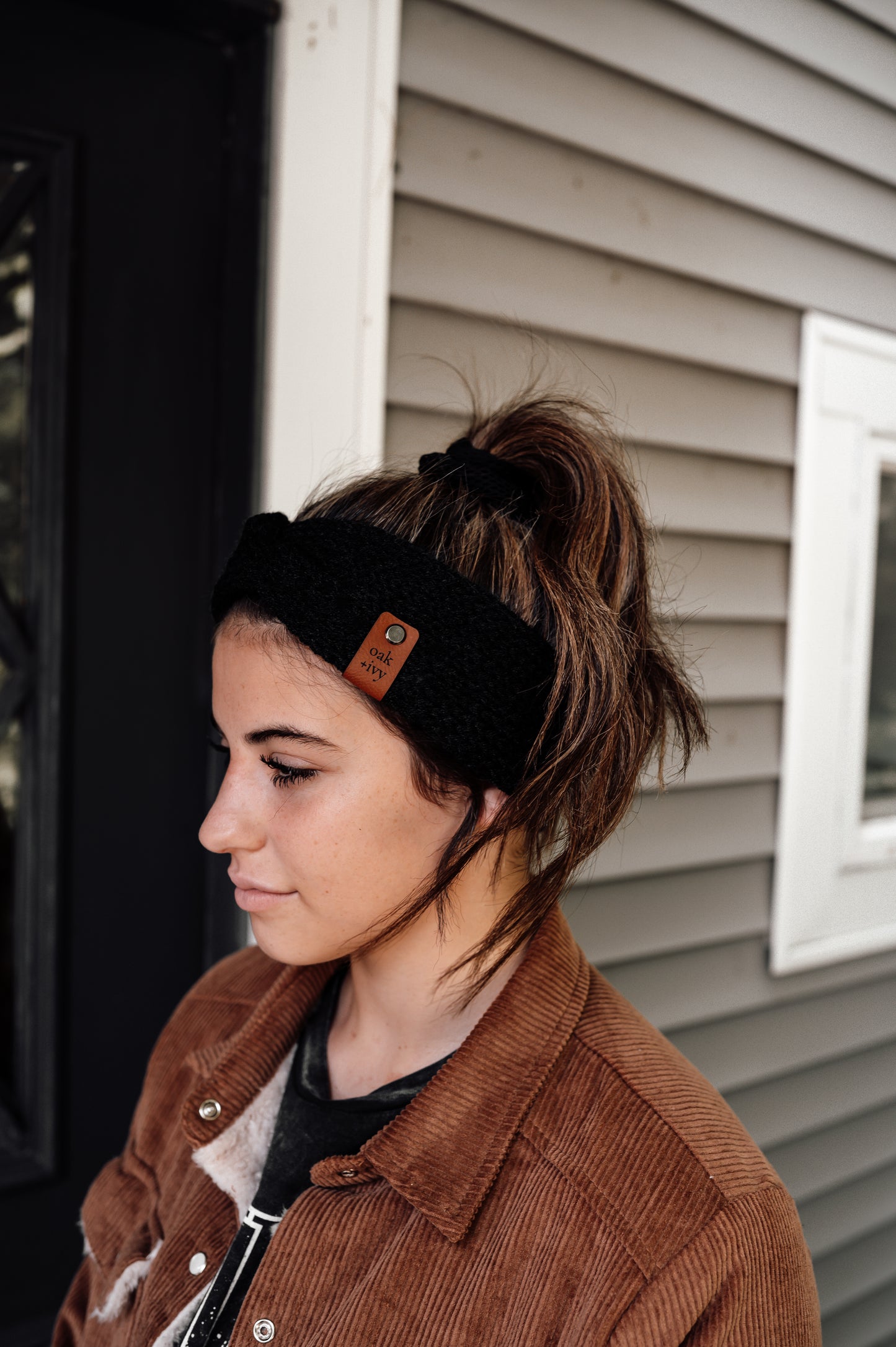 A person wearing a black knit headband with brand tag.