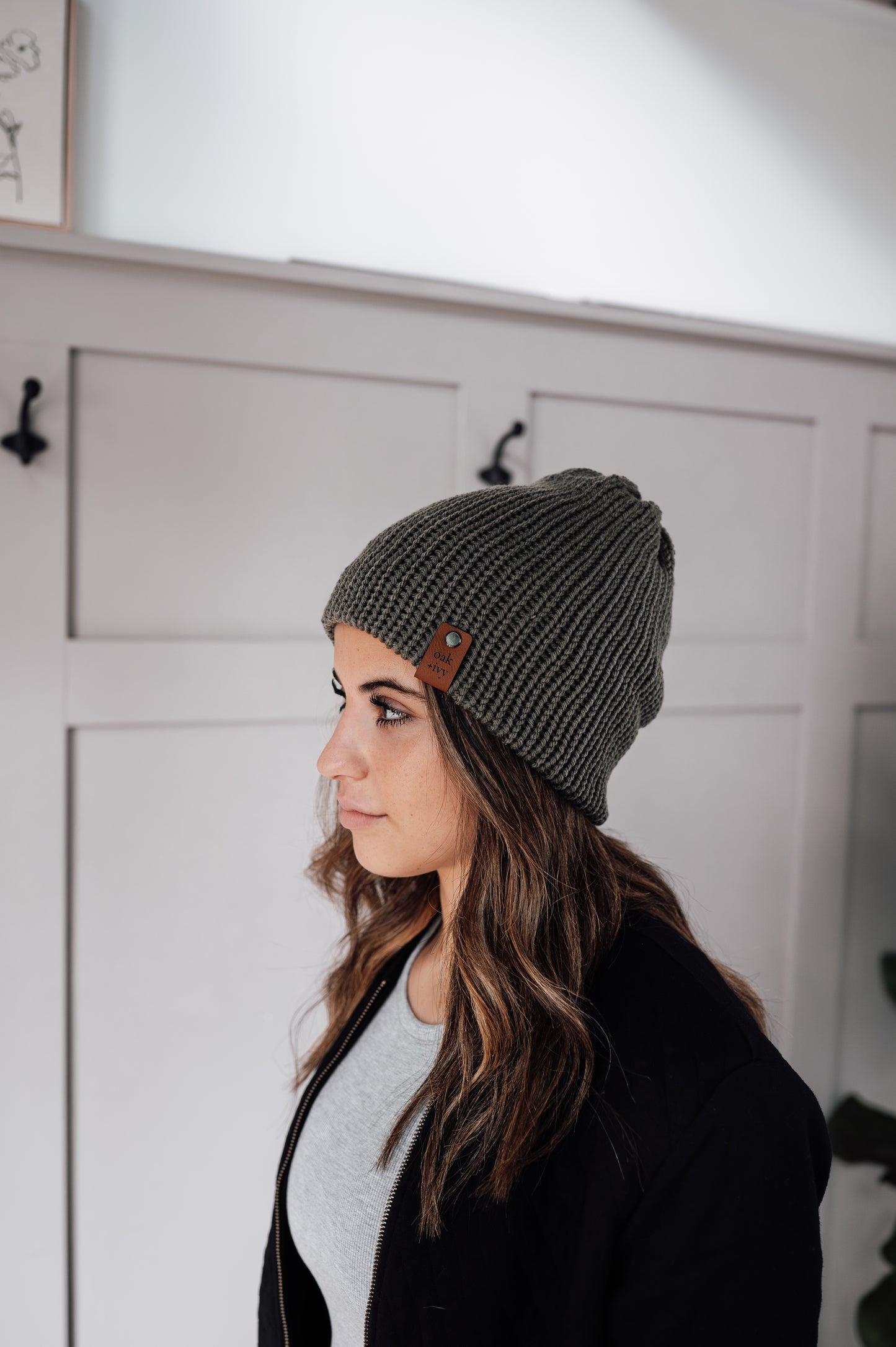 A person wearing an olive green knit beanie in a home environment.