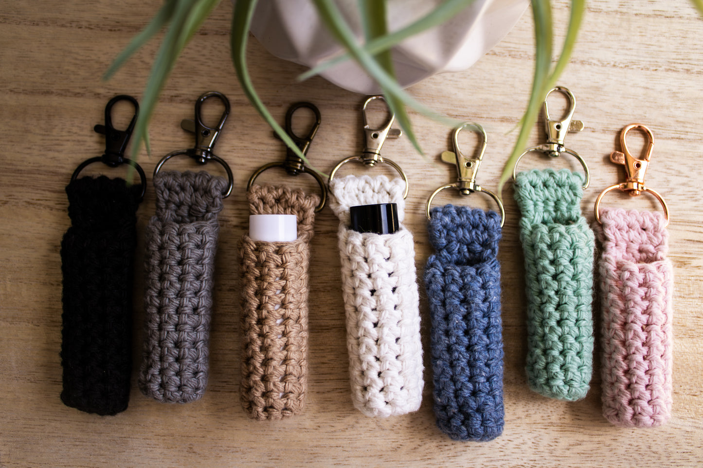 Set of crocheted chapstick holder keychains in various colors on a wooden surface.