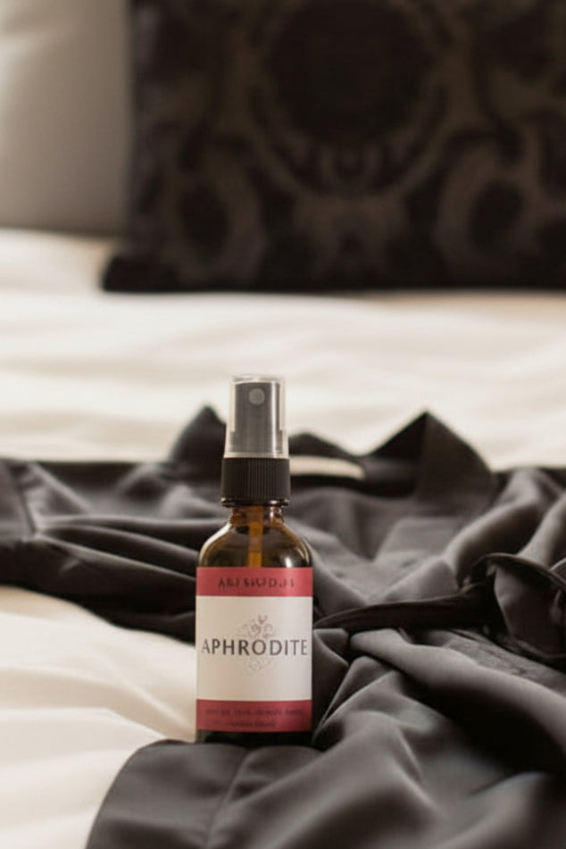 A bottle of K&G Naturals Aphrodite all-natural room spray on a white bed next to a black silky robe