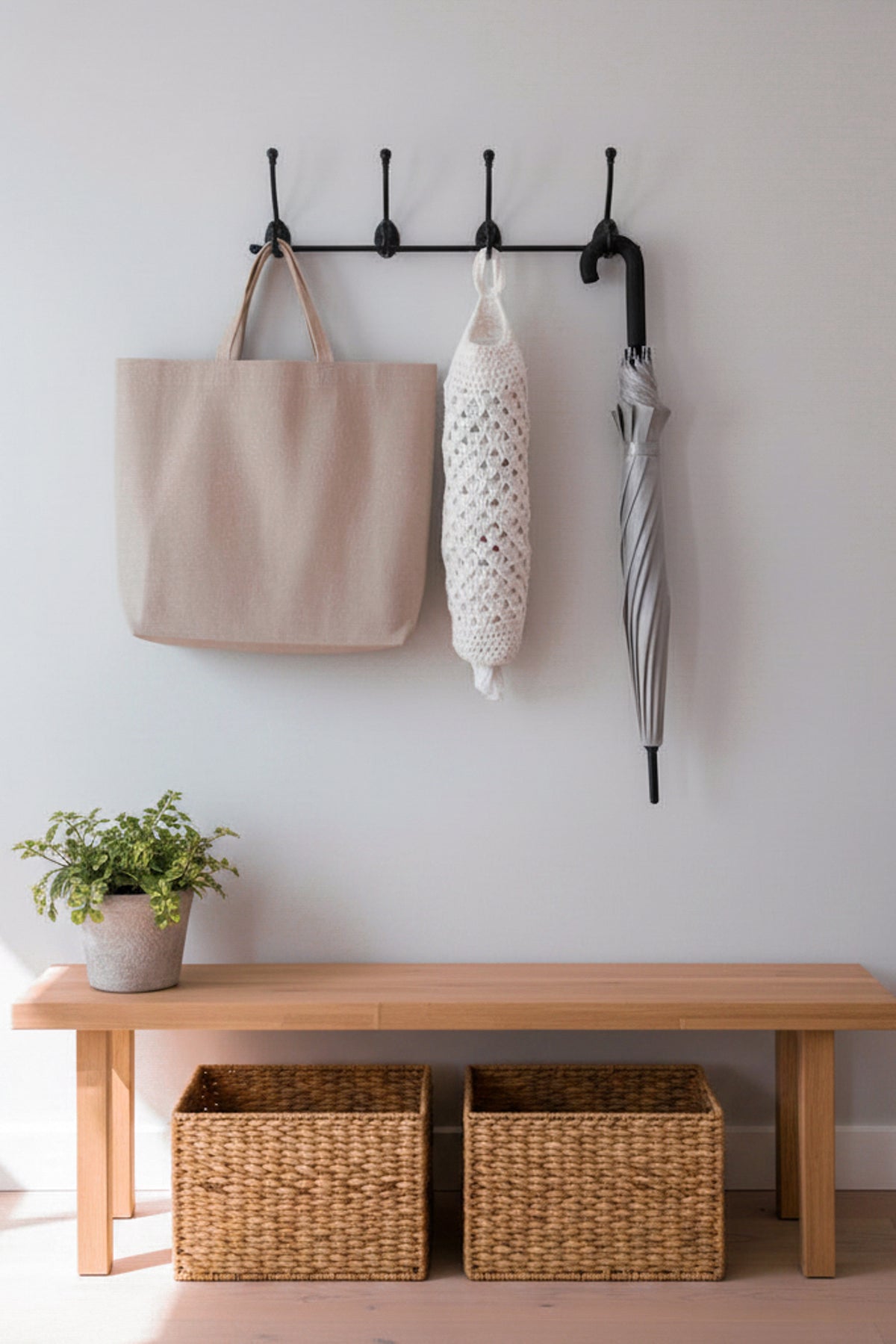 A handmade off-white crochet hanging bag saver with a loop at the top, hanging from a black wall hook against a plain gray wall next to a reusable shopping bag and umbrella in a mudroom.