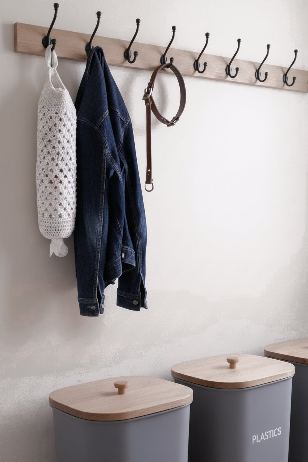 An off-white crocheted plastic bag saver hanging next to a denim jacket and dog collar over recycling bins in a mudroom.