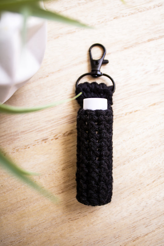 Black crocheted chapstick holder keychain with a white chapstick tube in it on a light wooden surface