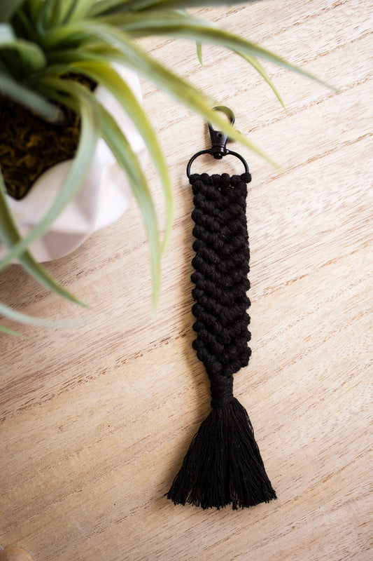Black braided keychain on a light wooden surface with a plant in the background