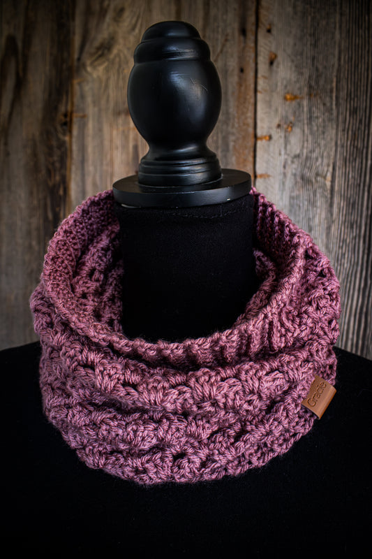 Rose colored crocheted scarf on a black mannequin against a wooden background