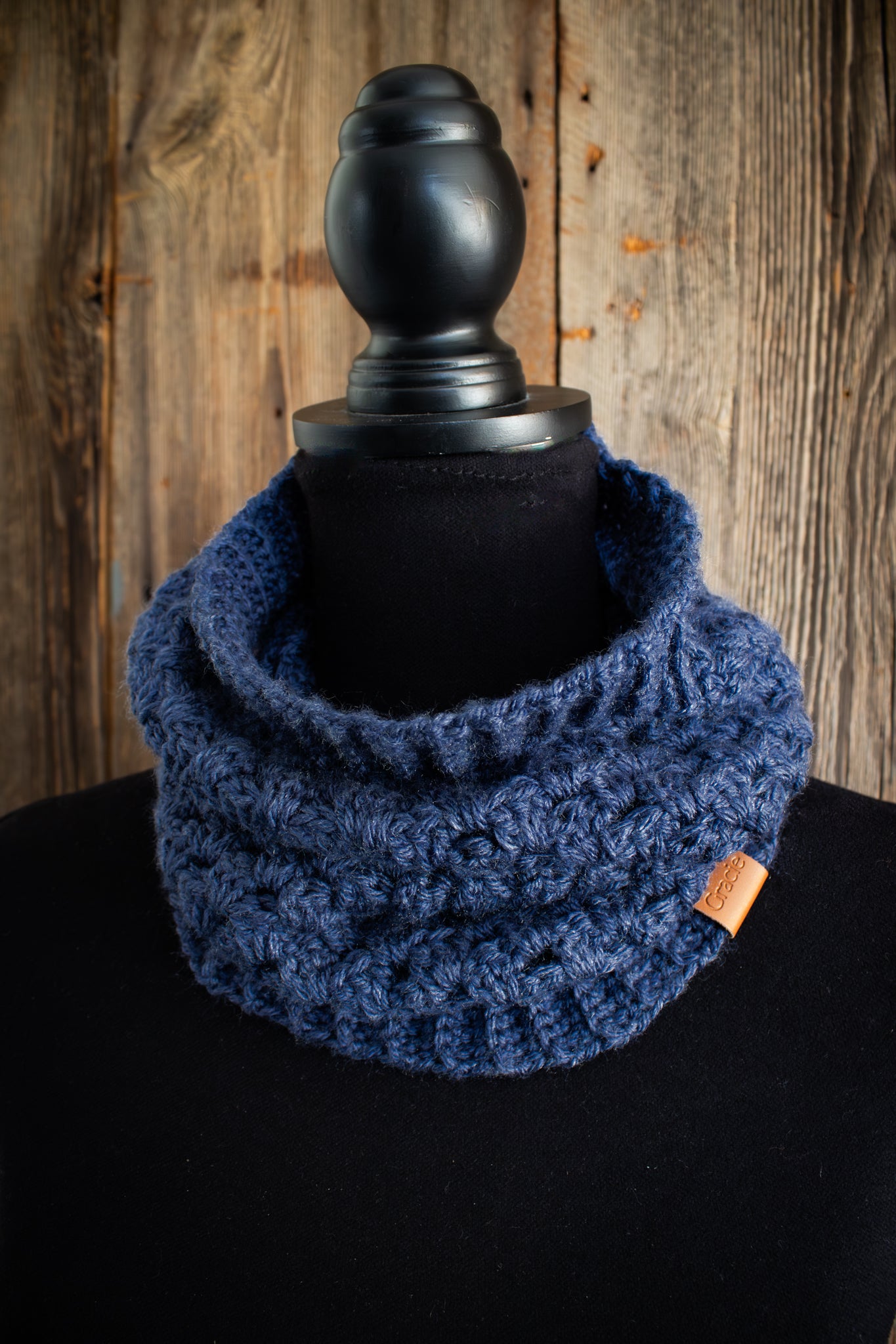 Blue crocheted cowl on a black mannequin against a wooden background