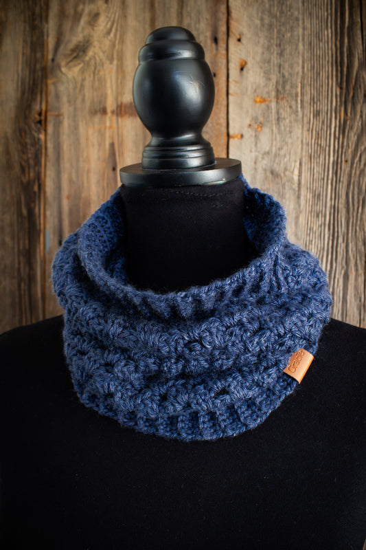 Blue crocheted cowl on a black mannequin against a wooden background