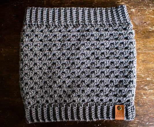 Gray crocheted cowl with a brand tag on a wooden surface
