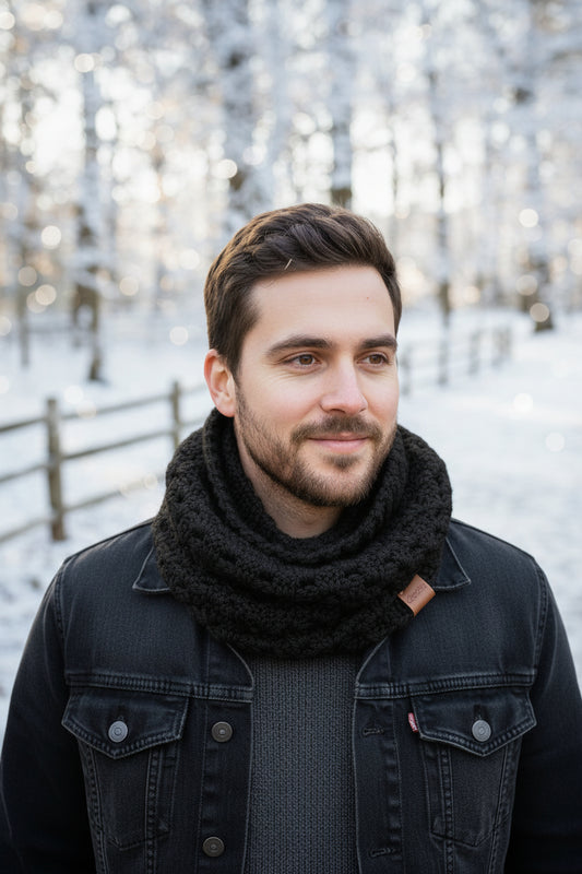 A crocheted cowl neck warmer in black on a man in a dark denim jacket and charcoal shirt in the Winter outdoors