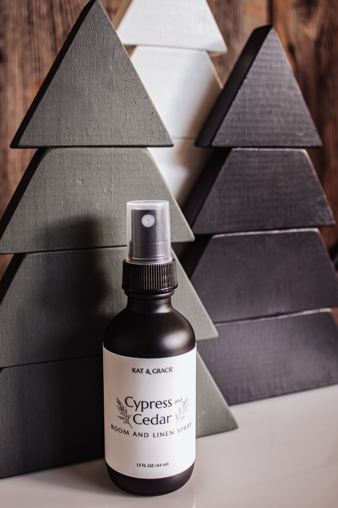 Bottle of Kat & Gracie Cypress and Cedar Room and Linen Spray against a wooden tree background.