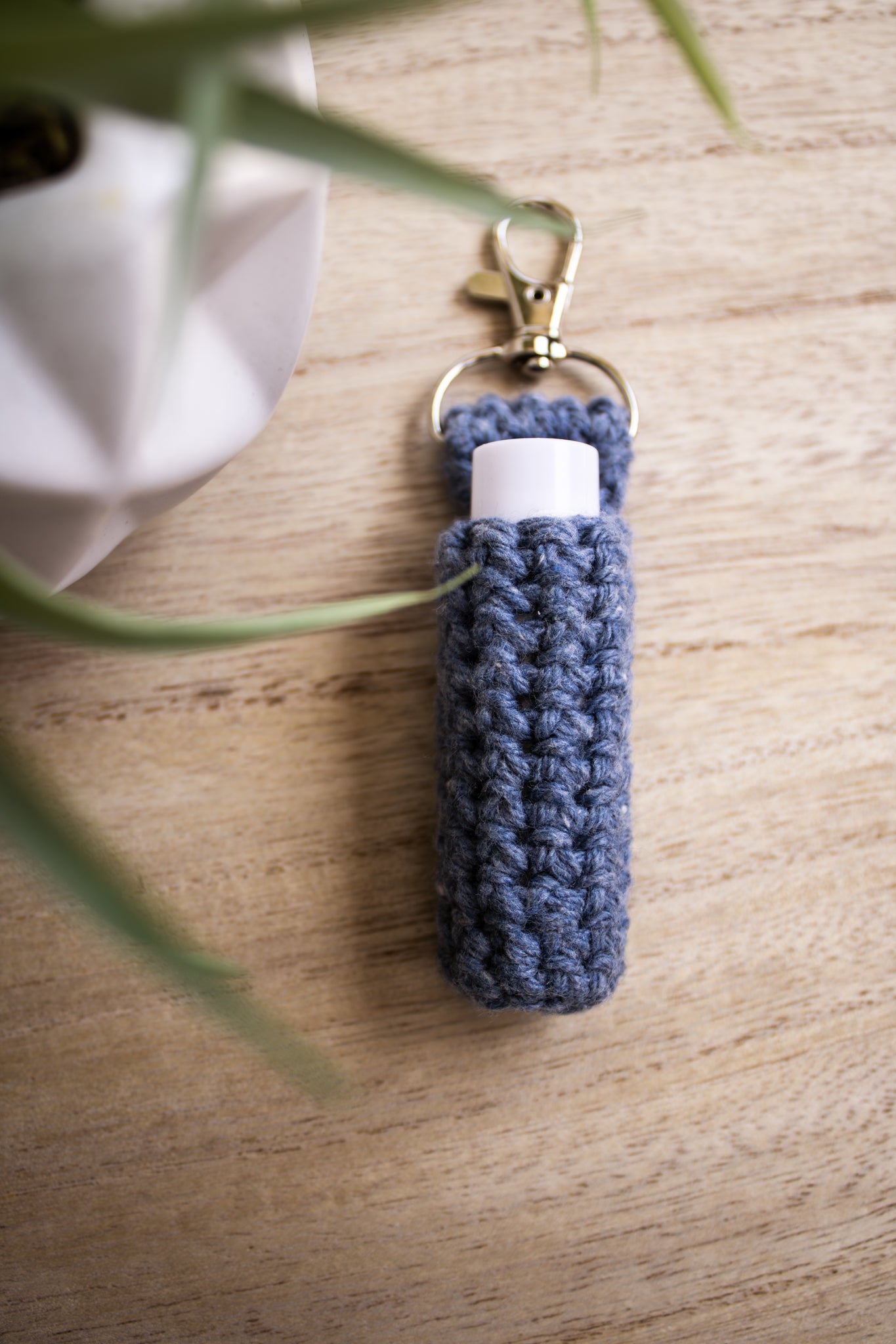 Denim blue crocheted chapstick holder keychain with a white chapstick tube in it on a wooden surface