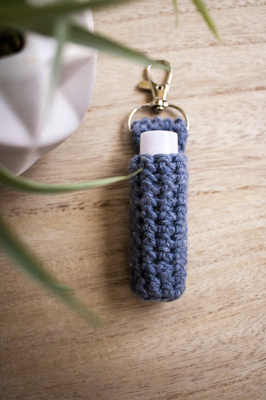 Denim blue crocheted chapstick holder keychain with a white chapstick tube in it on a wooden surface