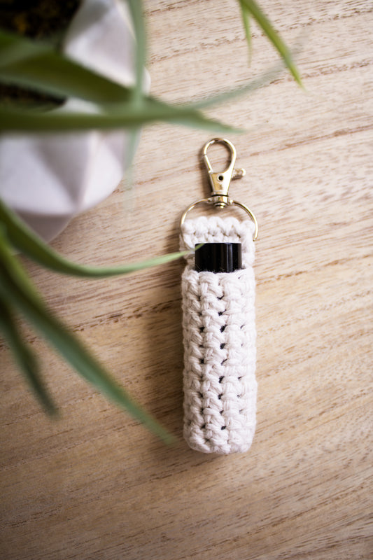 White crocheted chapstick holder keychain with a black chapstick tube in it on a wooden surface
