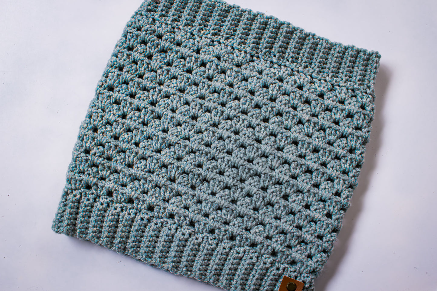 Blue-green colored crocheted cowl on a white background