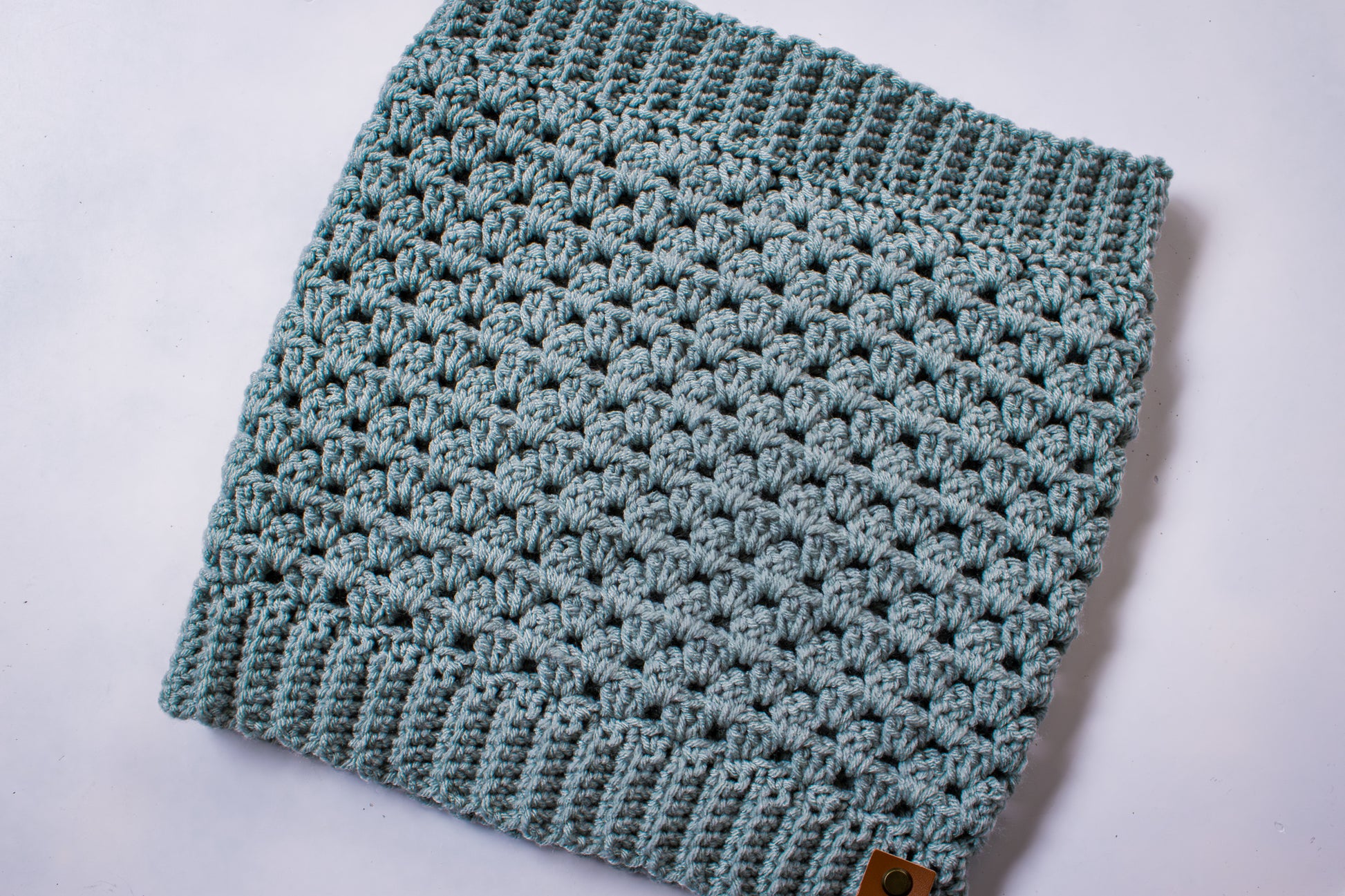 Blue-green colored crocheted cowl on a white background