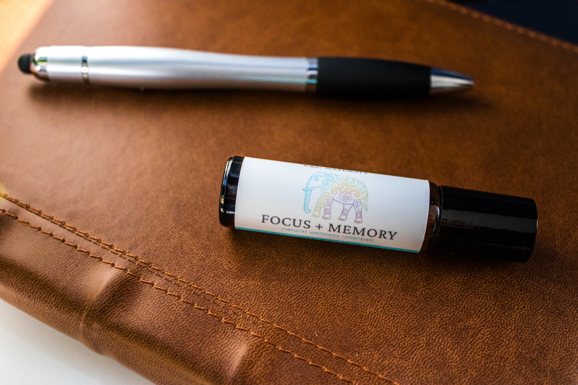 Roller bottle labeled 'Focus + Memory' on a brown leather surface with a pen.