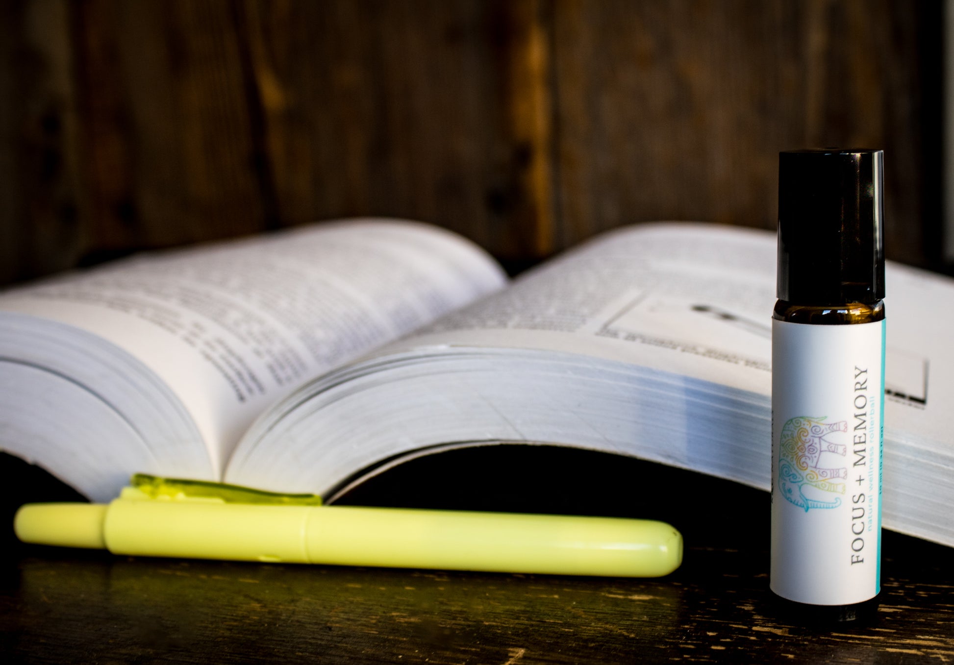 Roller bottle labeled 'Focus + Memory' next to an open book and highlighter on a wooden surface.