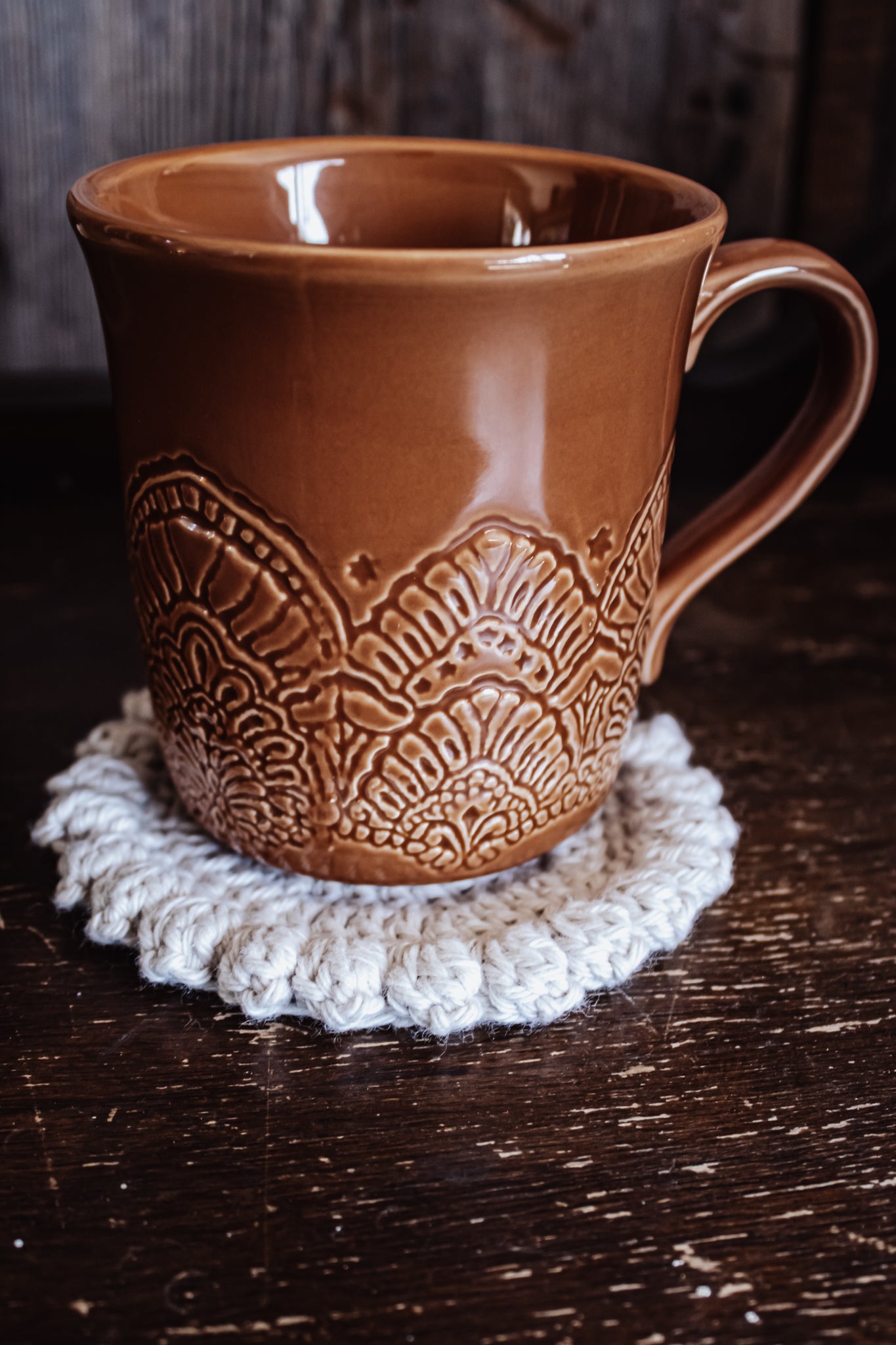 Brown ceramic mug with decorative patterns on an off-white crocheted coaster.