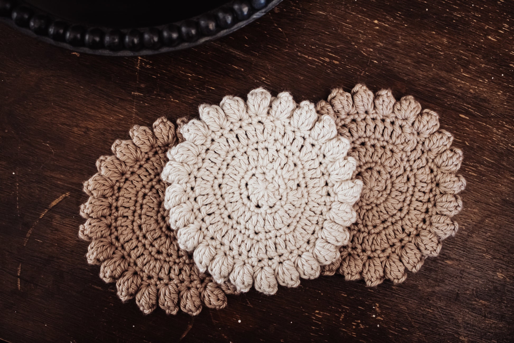 Three crocheted coasters on a wooden surface