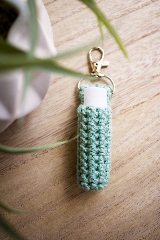 Jade green crocheted chapstick holder keychain with a white chapstick tube in it on a wooden surface