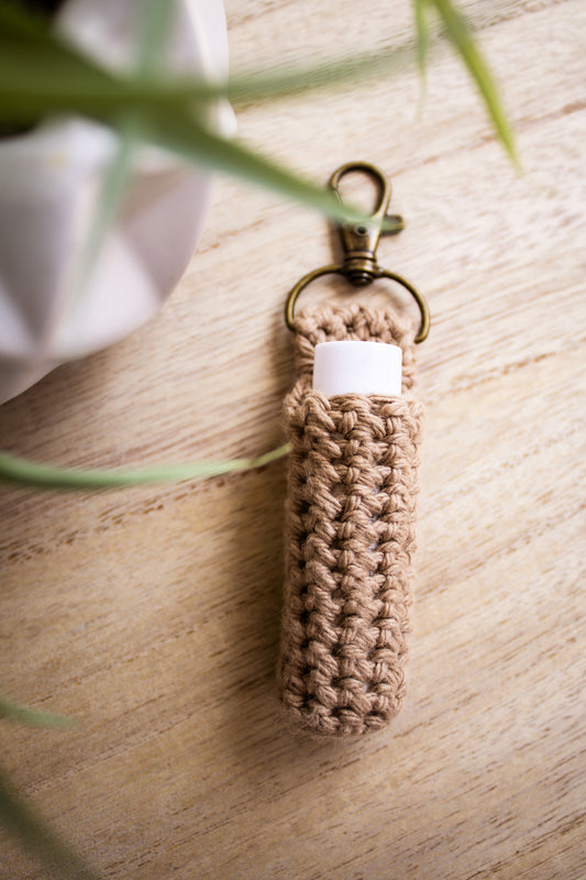 Jute crocheted chapstick holder keychain with a white chapstick tube in it on a wooden surface