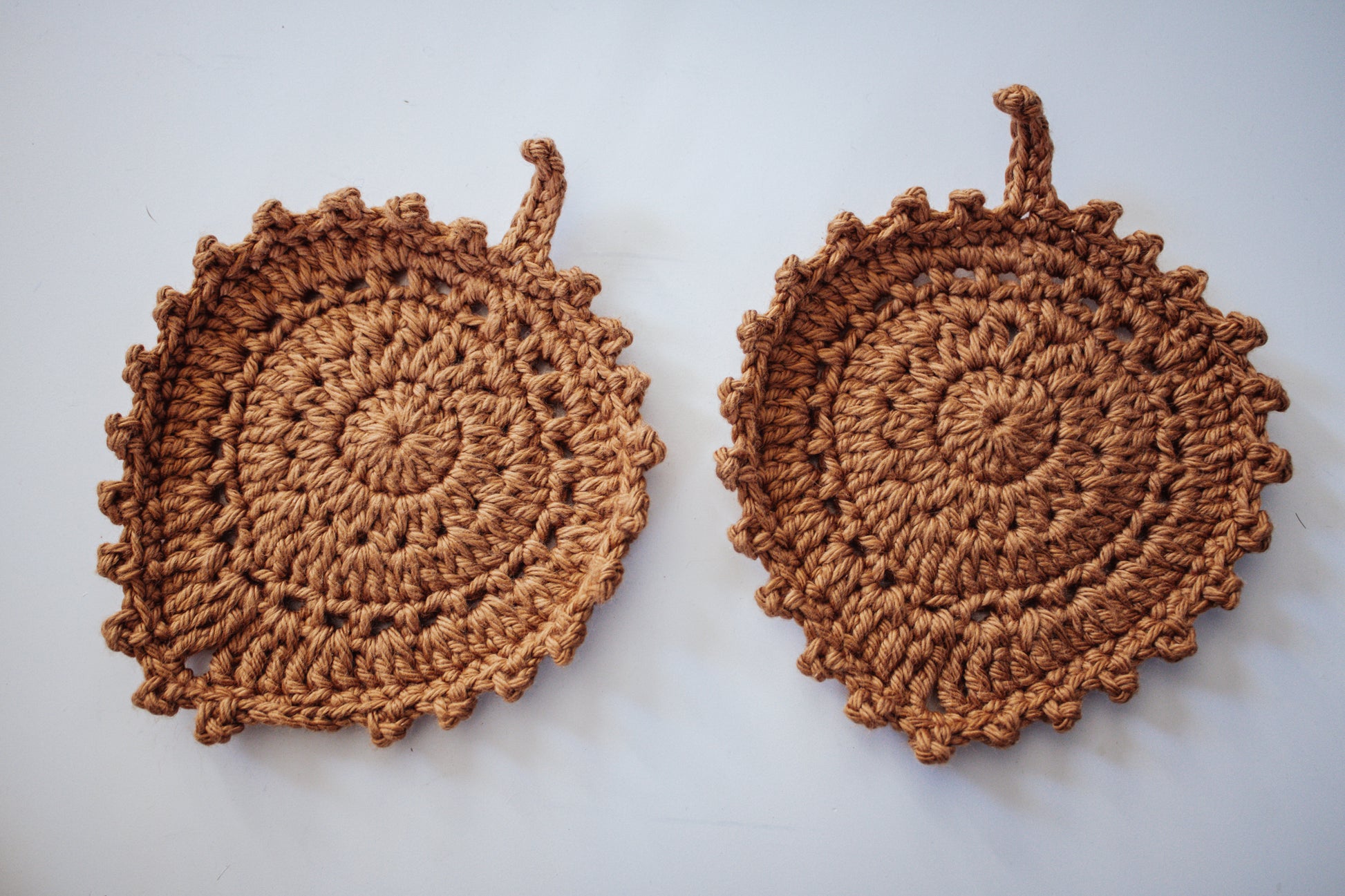 Two golden-colored crocheted coasters on a neutral background.