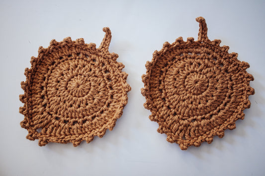 Two golden-colored crocheted coasters on a neutral background.