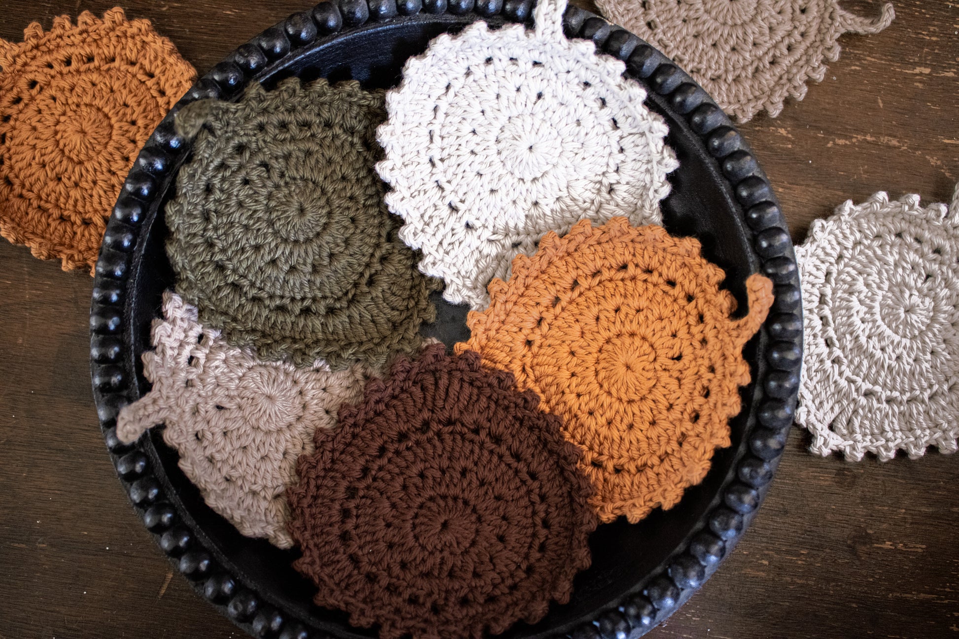 Collection of crocheted coasters in various colors on a wooden surface.