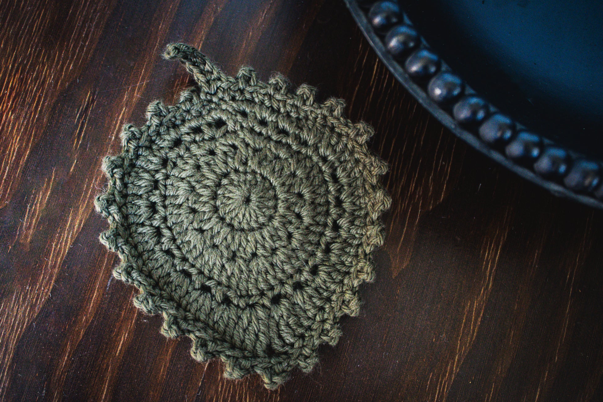 Olive green crocheted leaf coaster on a wooden surface