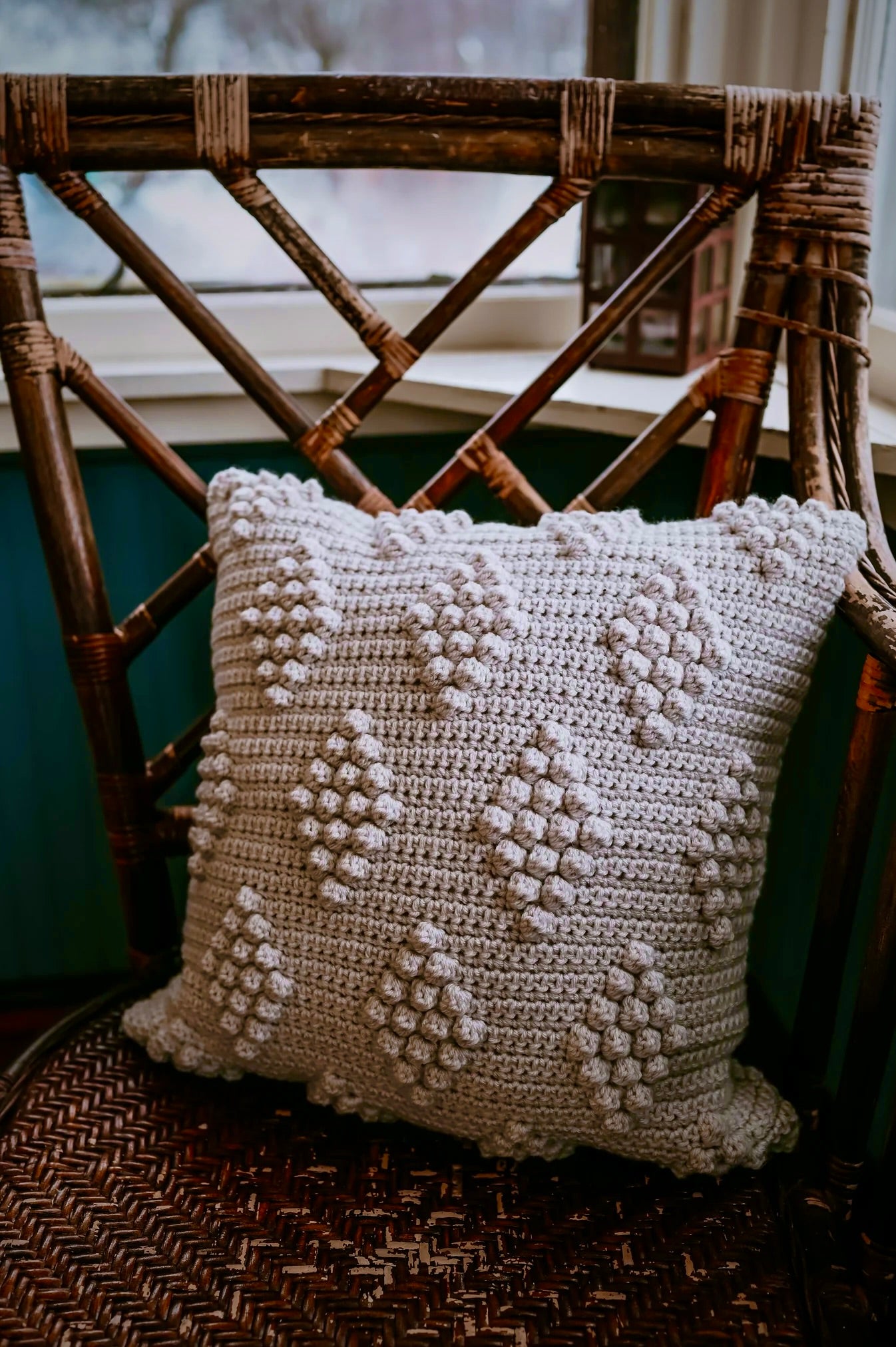 Crocheted pillow with a textured pattern on a wicker chair.