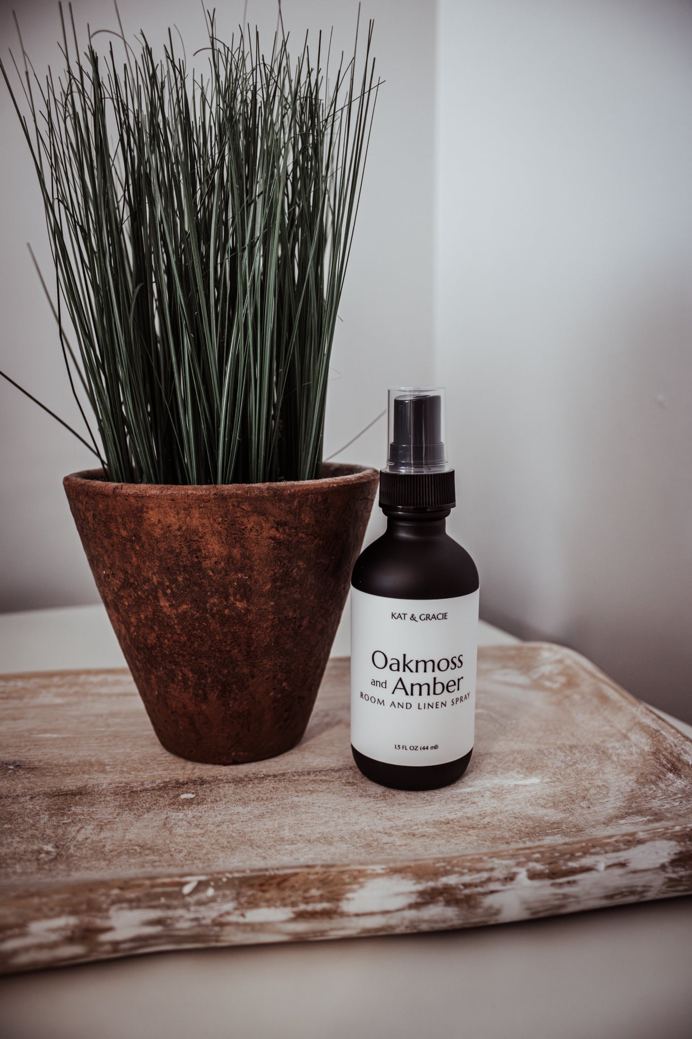 Bottle of 'Oakmoss & Amber' room spray next to a potted plant on a wooden surface.
