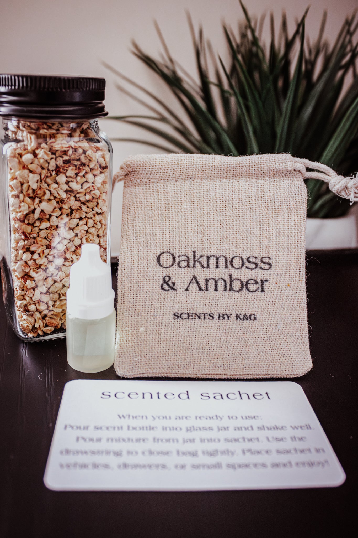 Scented sachet with Oakmoss & Amber branding, bottle, and jar on a dark surface.