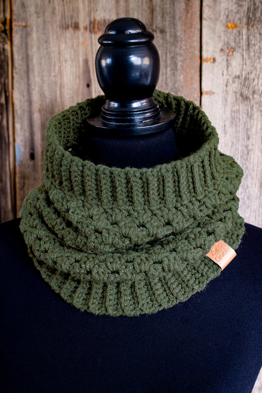 Crocheted cowl with leather brand tag on a mannequin with a wood background.