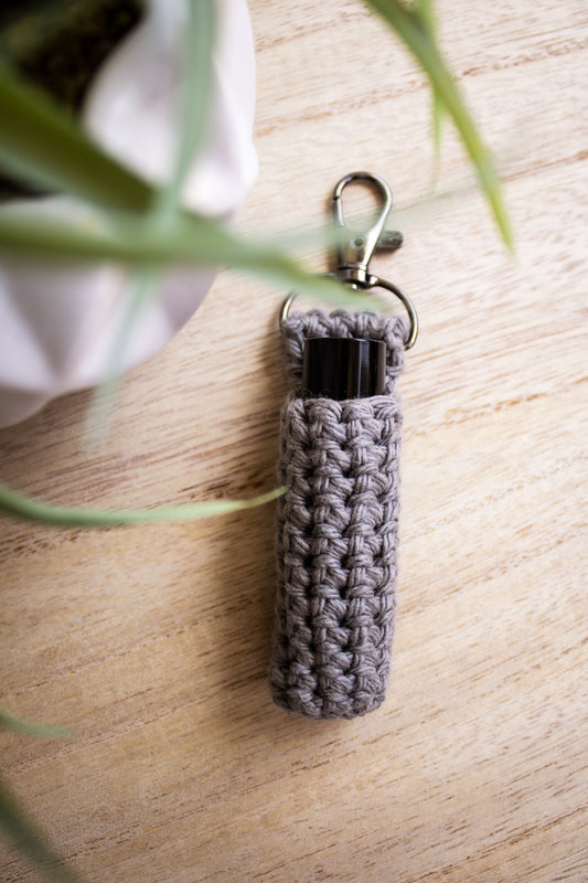 Grey crocheted chapstick holder keychain on a wooden surface with a black chapstick tube in it