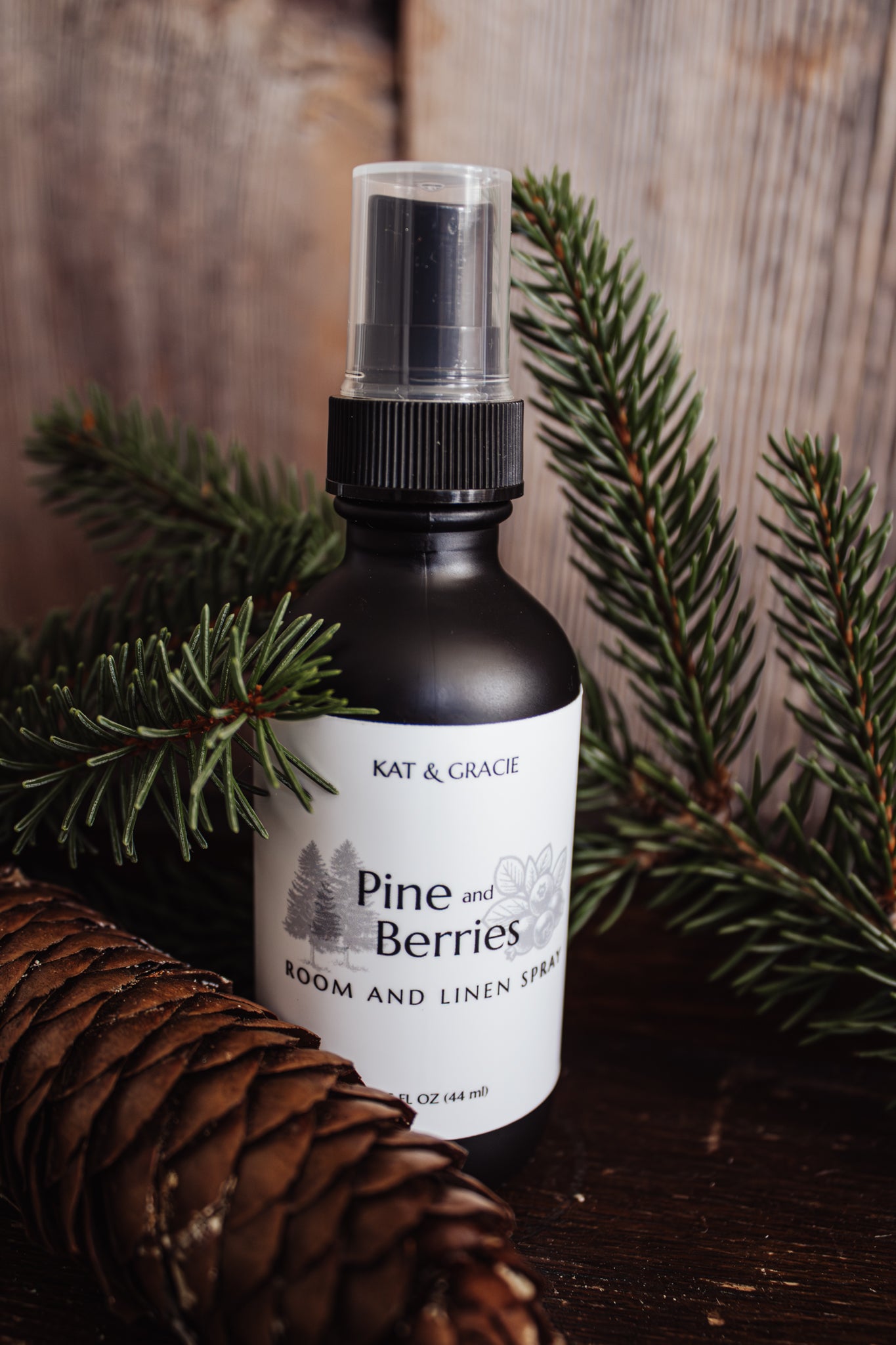 Bottle of 'Pine and Berries' room and linen spray with a pine cone and branches on a wooden background