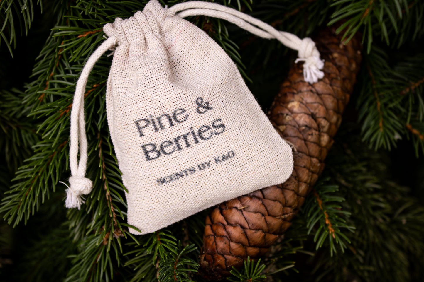 Small drawstring bag labeled 'Pine & Berries' on a pine branch with a pine cone.