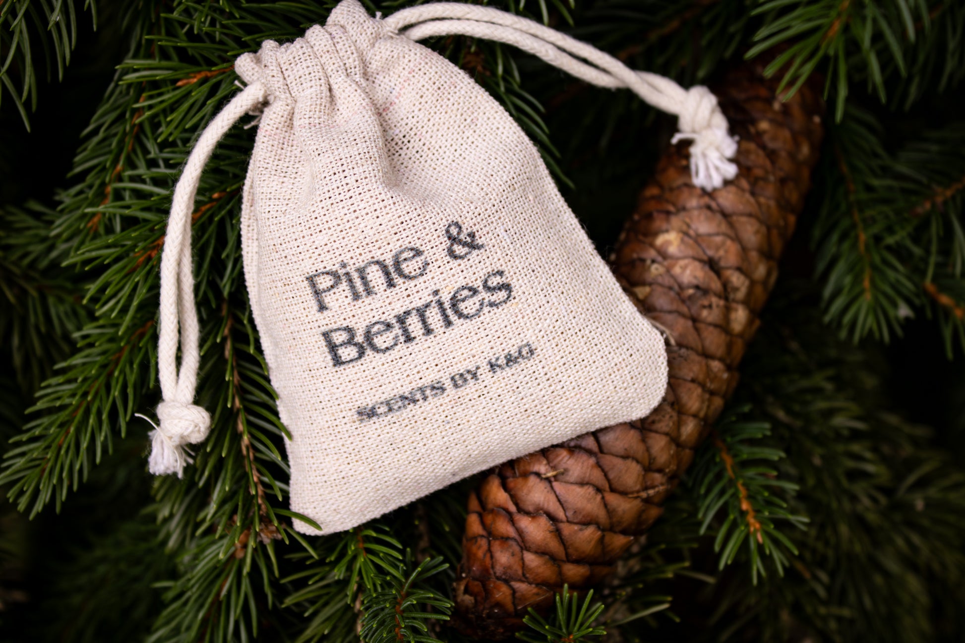 Small drawstring bag labeled 'Pine & Berries' on a pine branch with a pine cone.