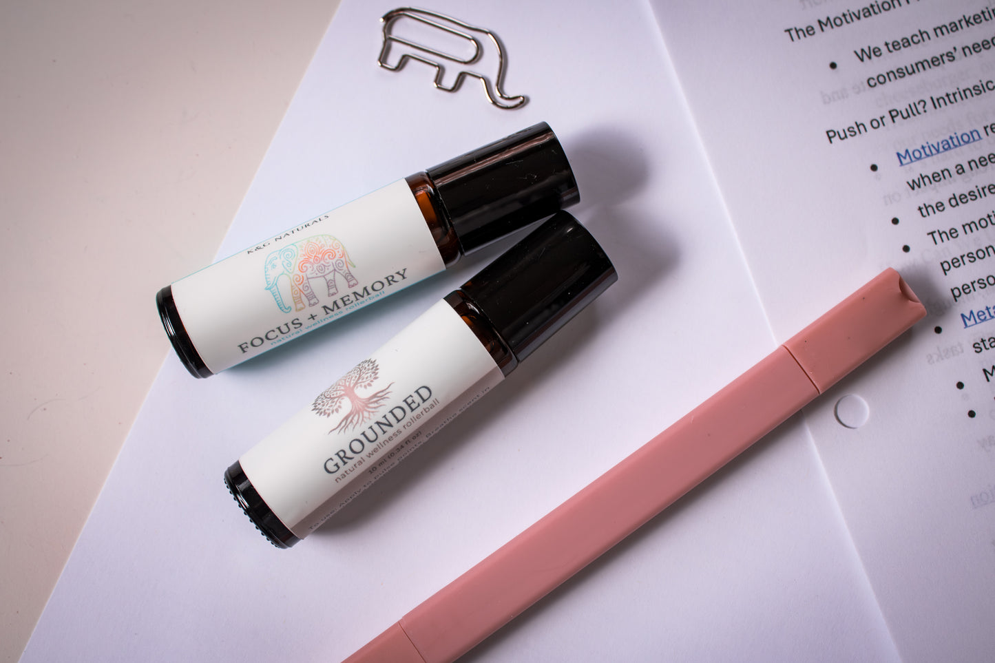 Two rollerball bottles labeled 'Focus + Memory' and 'Grounded' on a stack of papers with a pink highlighter