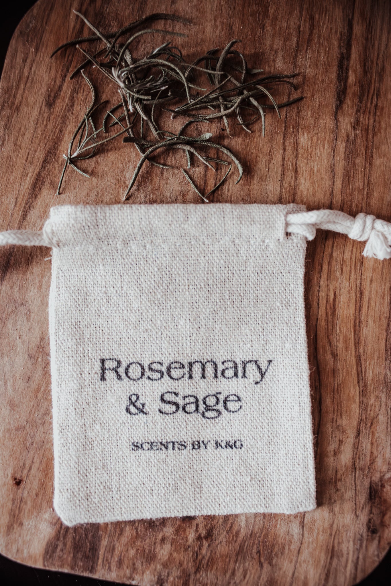 Small fabric pouch labeled 'Rosemary & Sage' with dried herbs on a wooden surface