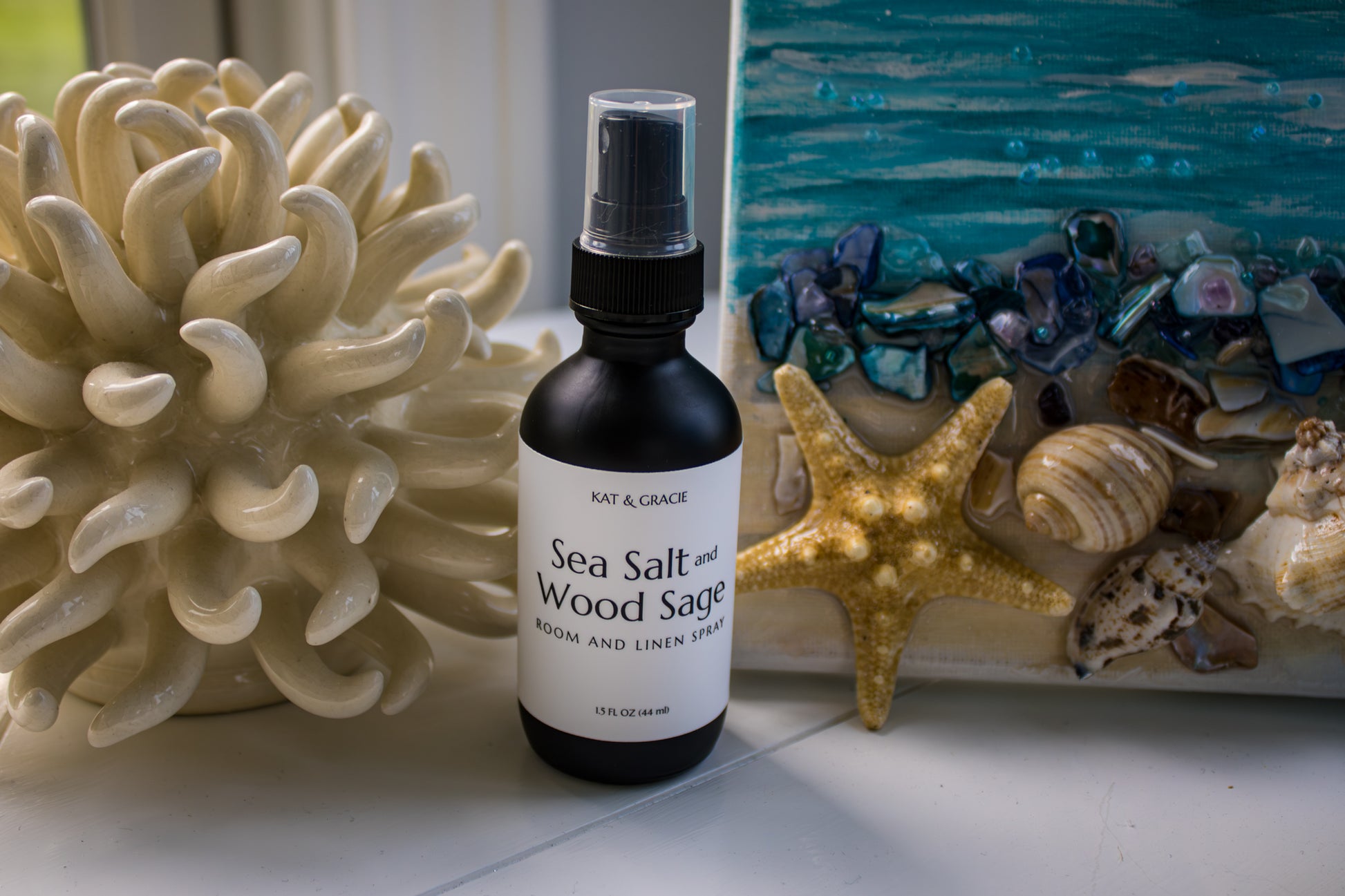 Bottle of 'Sea Salt and Wood Sage' room spray with coral and starfish decor in the background