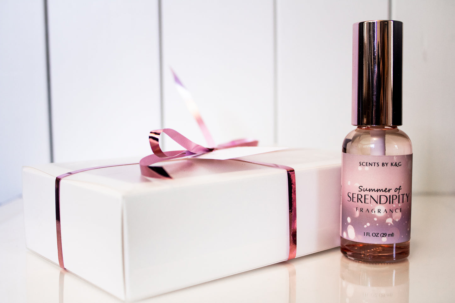 Perfume bottle labeled 'Summer of Serendipity' next to a white gift box with a pink ribbon on a light background.