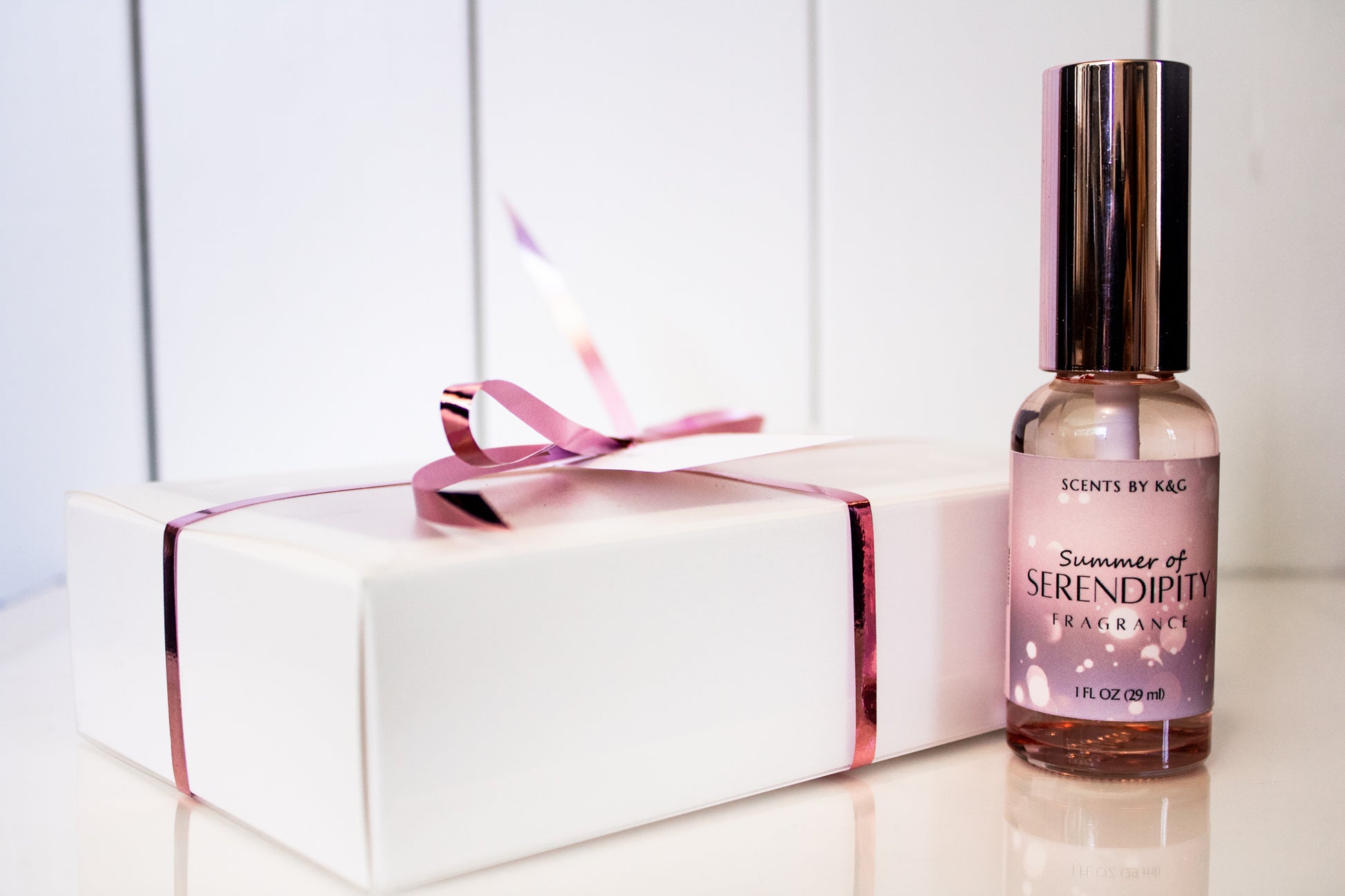 Perfume bottle labeled 'Summer of Serendipity' next to a white gift box with a pink ribbon on a light background.