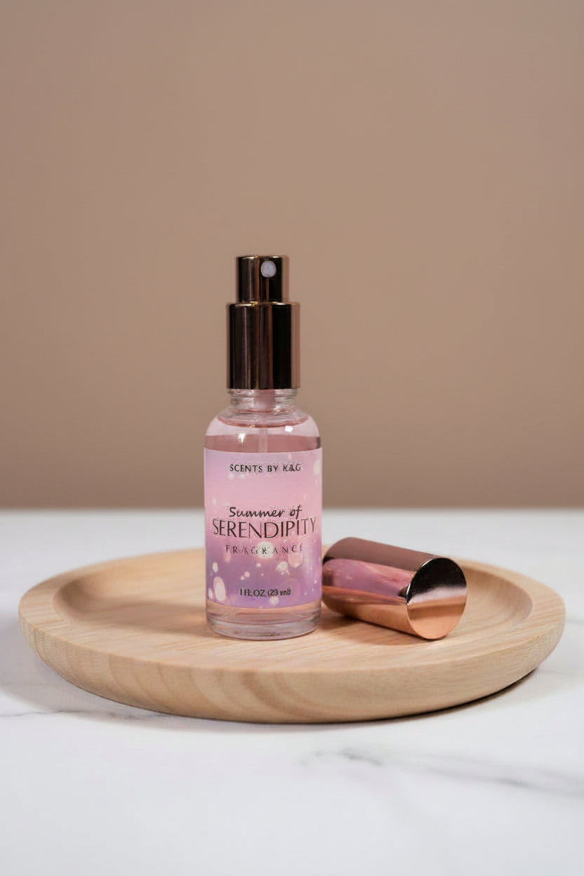 A bottle of Scents by K&G fragrance labeled 'Summer of Serendipity Fragrance' with a metallic rose gold cap removed on a wood surface against a soft mauve background