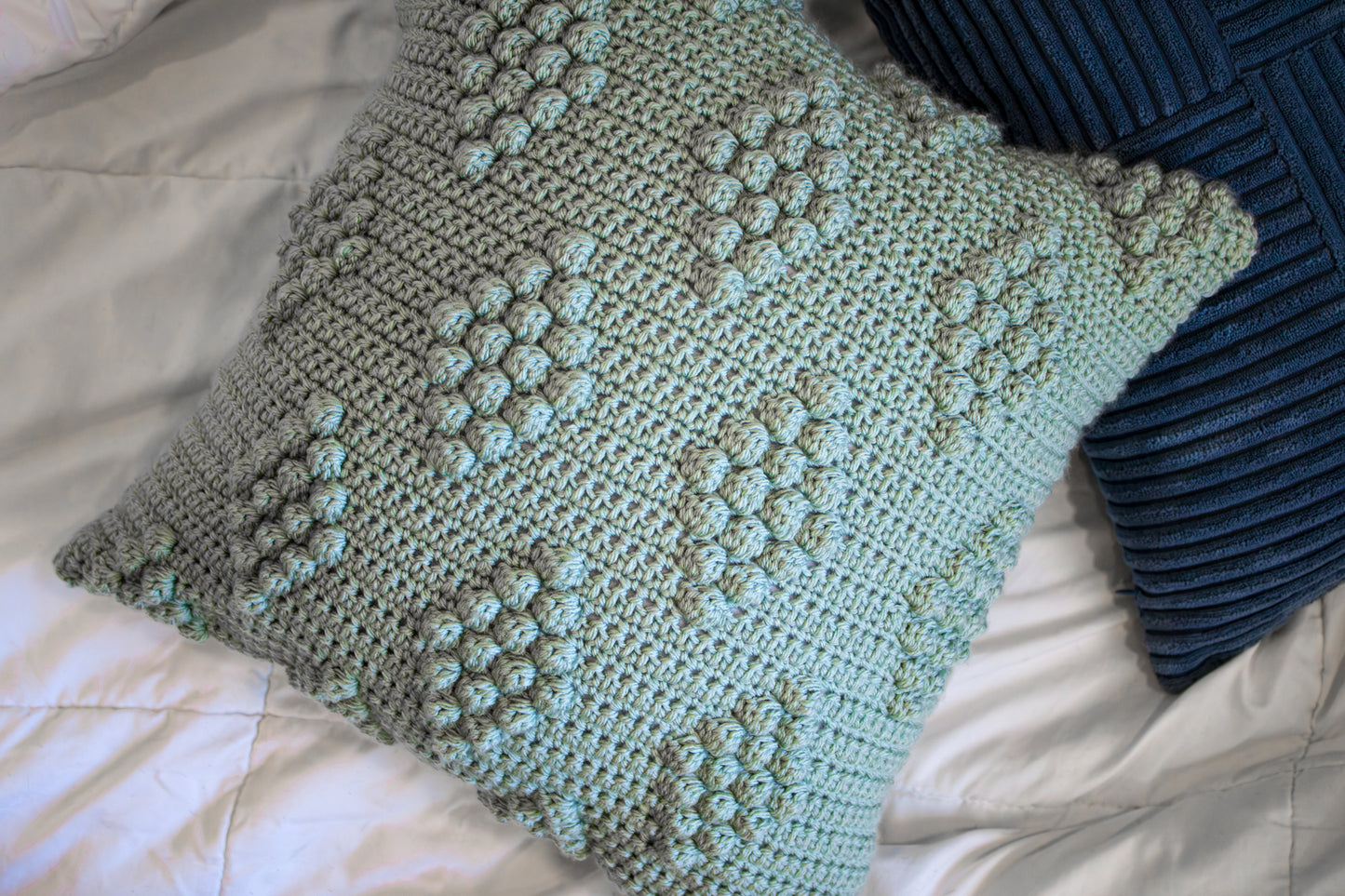 Crocheted pillow with a diamond pattern on a bed