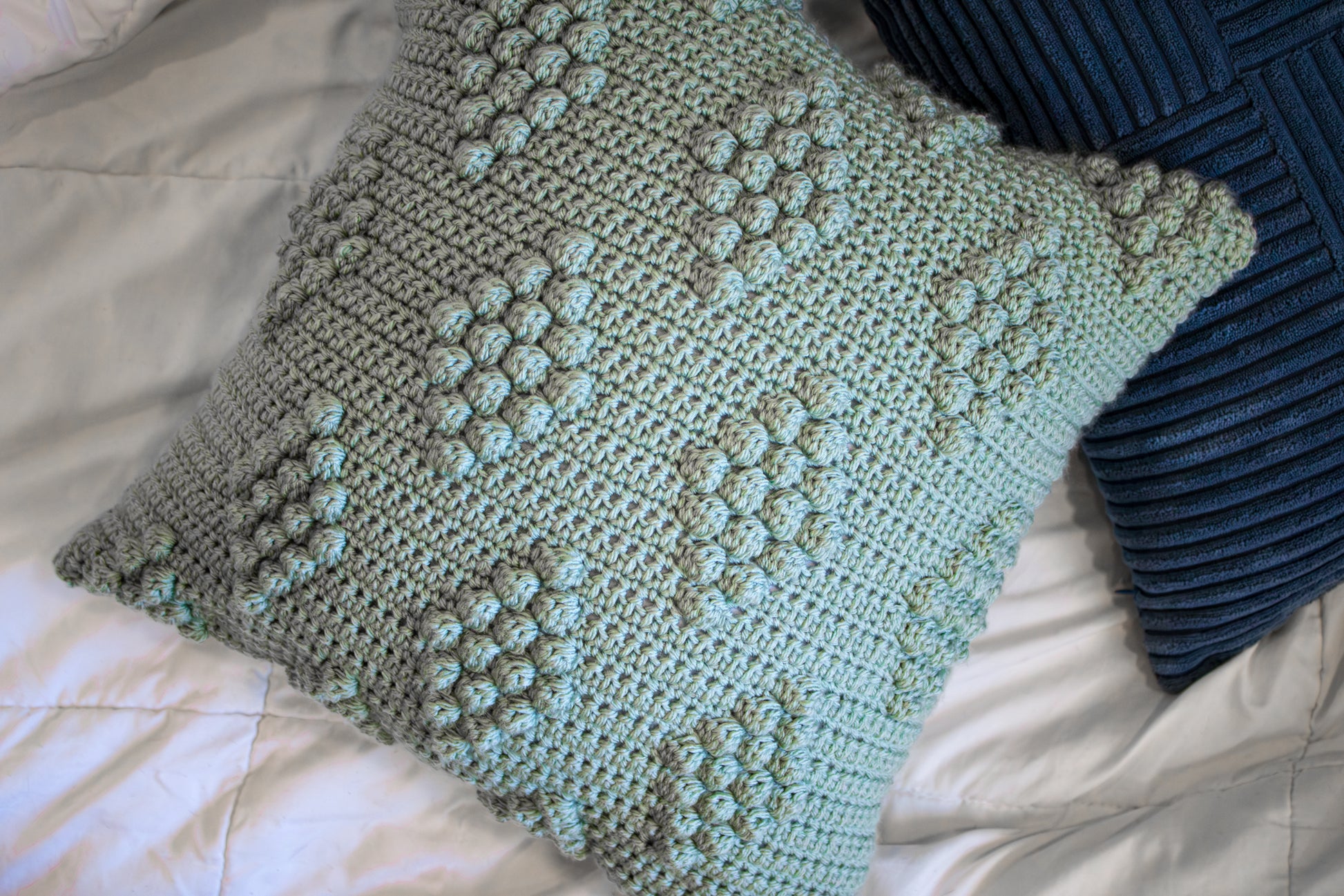 Crocheted pillow with a diamond pattern on a bed