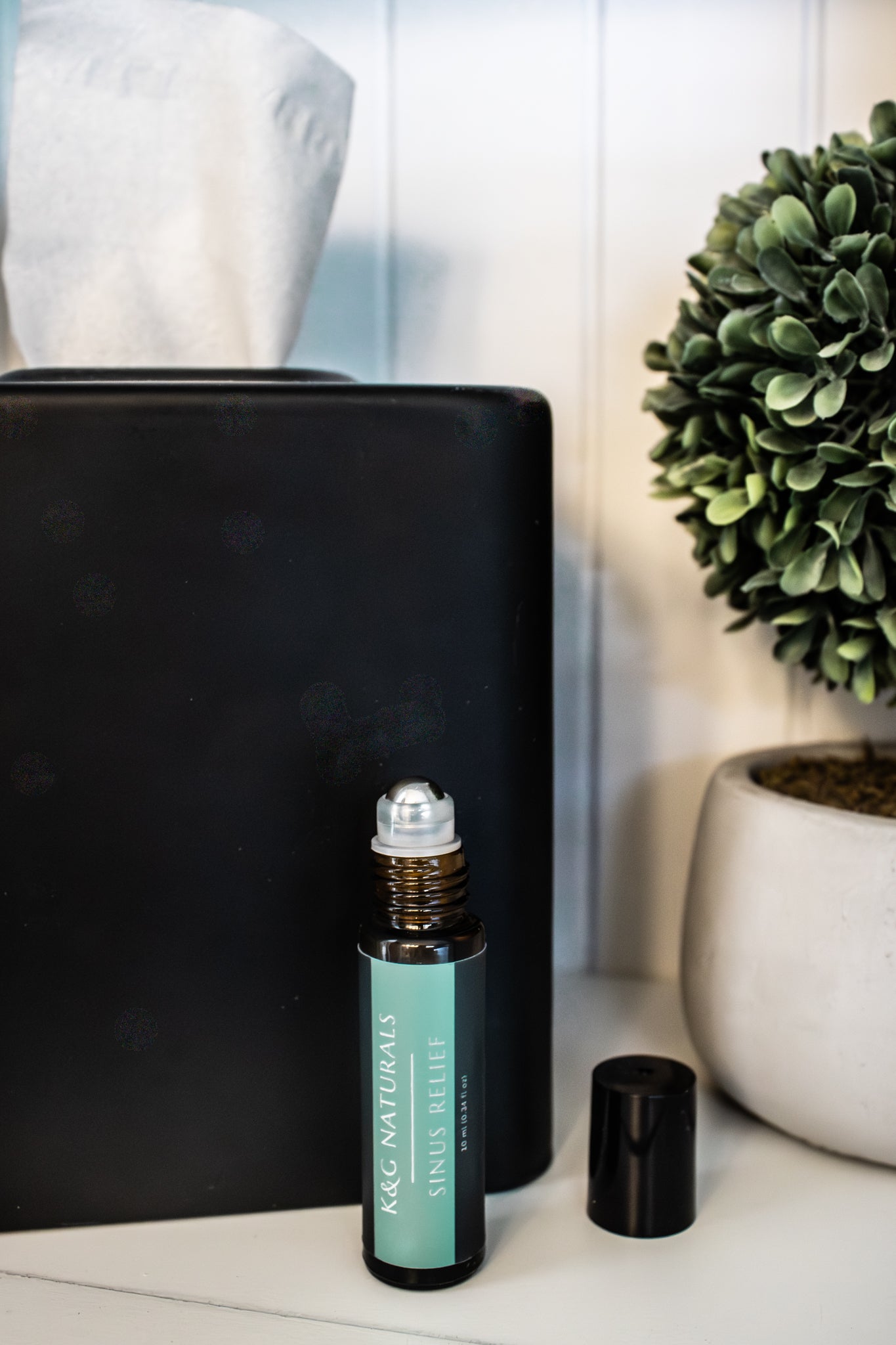 K&G Naturals Sinus Relief roller bottle on a shelf with a tissue and plant in the background